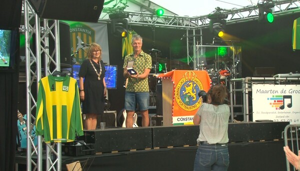 De uitreiking van de koninklijke erepenning door burgemeester Marieke Moorman aan W.V.V. Constantia voorzitter Marco Verheijen (foto: still Omroep Land van Cuijk)
